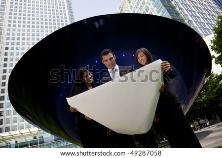 A mixed race team of one man, an Indian and Chinese Asian woman looking at an architectural plan outside in a modern city environment