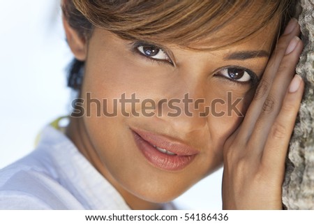 Portrait of a beautiful mixed race woman outside resting on a palm tree
