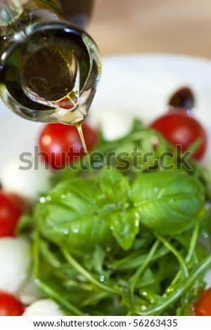 Close up macro photograph of olive oil dressing being poured onto a fresh rocket and basil salad with cherry tomatoes and balsamic vinegar
