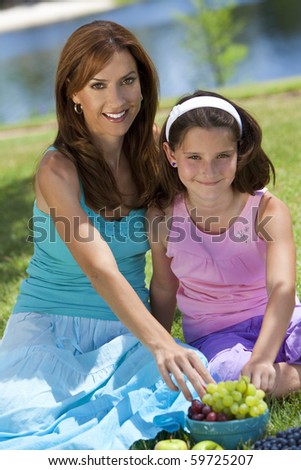 Woman and girl, mother and daughter, together outside in the countryside eating healthy fruit at a picnic by a lake