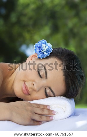 Portrait of a beautiful young Latina Hispanic woman laying down outside relaxing at a health spa with a blue flower in her hair