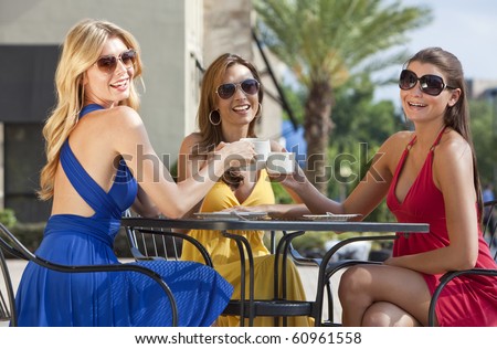 Three beautiful and sophisticated young women friends wearing sunglasses and having coffee around a modern city cafe table