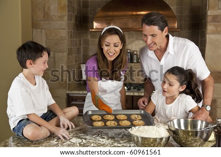 An attractive smiling family of mother, father, and two children baking and eating fresh chocolate chip cookies in a kitchen at home