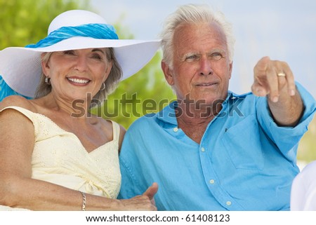 Happy senior man and woman couple sitting together pointing out to sea on a deserted tropical beach
