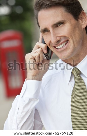 A successful businessman talking on his cell phone in London, England, with a classic red telephone box out of focus behind him