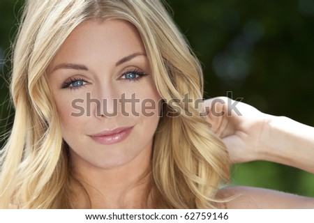 Portrait of naturally beautiful woman in her twenties with blond hair and blue eyes, shot outside in sunlight with a natural green background