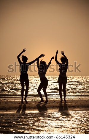 Three beautiful young women in bikinis dancing on a beach at sunset all in silhouette