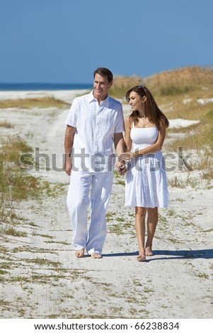 Man and woman romantic couple in white clothes holding hands and walking on a deserted tropical beach with bright clear blue sky