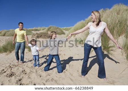 A happy family of mother, father and two sons, walking holding hands and having fun in the sand dunes of a sunny beach