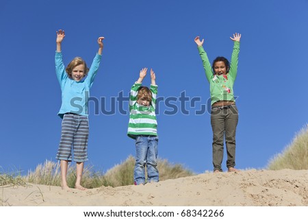Three children, two blond boys and a mixed race little girl, having fun arms raised in the dunes of a sandy beach
