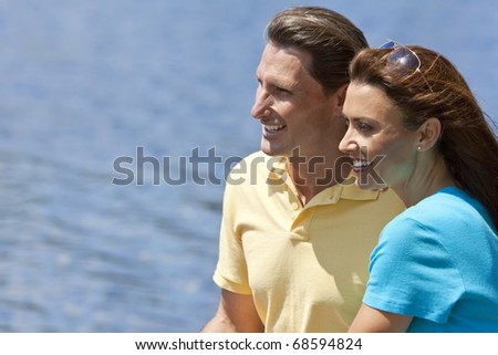 Portrait shot of an attractive, successful and happy middle aged man and woman couple in their thirties, sitting together outside smiling with a natural water background.