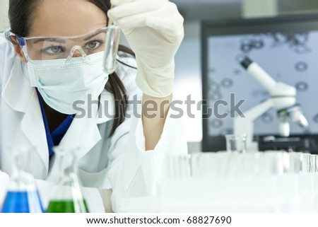 A female medical or scientific researcher or woman doctor looking at a test tube of clear solution in a laboratory with her microscope beside her.