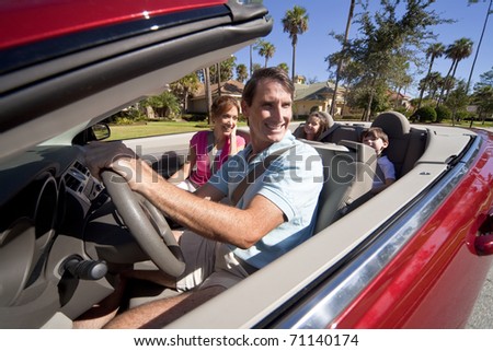 Man and woman parents and two children having fun driving in a red convertible car in sunshine