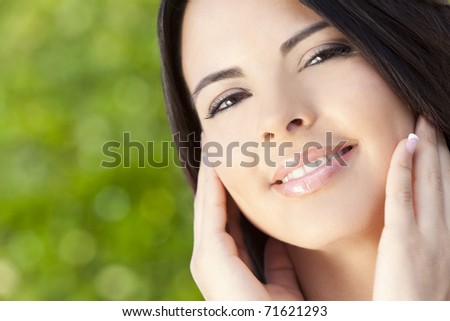 Outdoor portrait of a beautiful young Latina Hispanic woman hands on her face and with natural green background