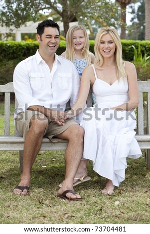 A happy young family of mother father and girl child sitting outside on a park bench on a sunny summer day.