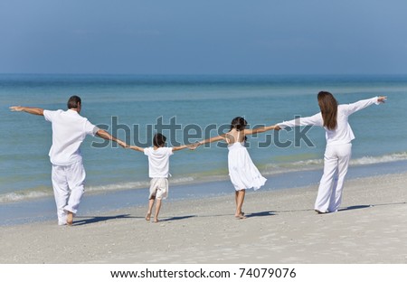 Rear view of a happy family of mother, father and two children, son and daughter, running holding hands and having fun in the sand of a sunny beach