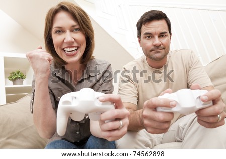 Man and woman married couple having fun playing computer console game together, the woman is celebrating winning the man is upset losing