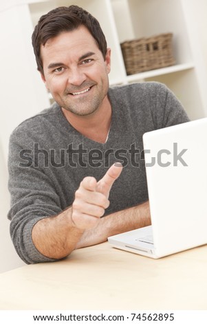 Smiling man in his thirties at home using his laptop computer and pointing to camera