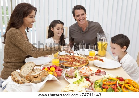 An attractive happy, smiling family of mother, father, son and daughter eating salad and pizza at a dining table, The mother is serving a slice of pizza to the excited boy.