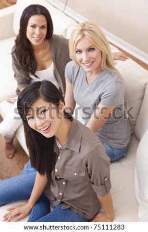 Interracial group of three beautiful young women friends at home sitting together on a sofa smiling and having fun