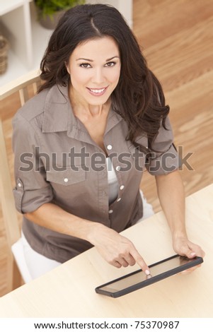 Overhead photograph of a happy beautiful young woman sitting at home using a tablet computer