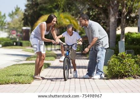 A young African American family with boy child riding his bicycle and his happy excited parents encouraging him.