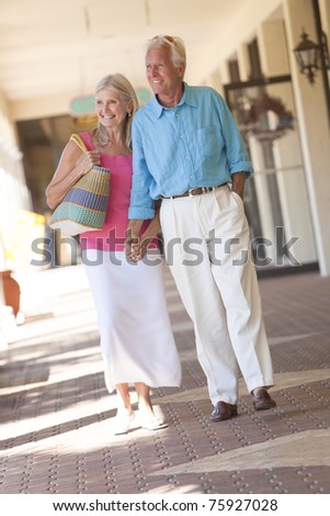 Happy senior man and woman couple holding hands and walking through a sunlit shopping mall
