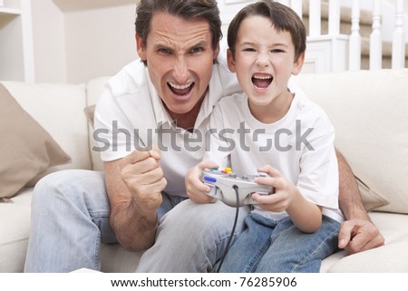 Happy man and boy, father and son, having fun playing video console games together, the young boy has the handset controller while dad is cheering.