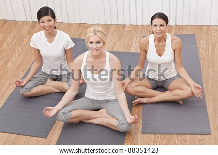 An interracial group of three beautiful young women sitting cross legged in a yoga position at a gym