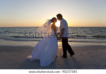 A married couple, bride and groom, kissing at sunset on a beautiful tropical beach