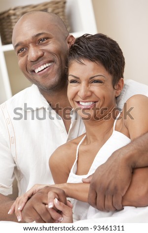A happy African American man and woman couple in their thirties sitting at home together smiling.