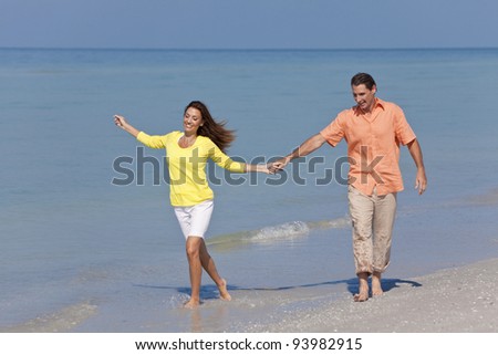 Man and woman romantic couple running holding hands on a deserted tropical beach with bright clear blue sky