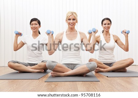 An interracial group of three beautiful young women sitting cross legged in a yoga position at a gym and weight training