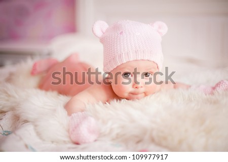 newborn baby girl in pink knitted bear hat lies at fur