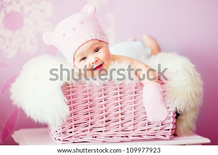 newborn baby girl in pink knitted bear hat lies at basket