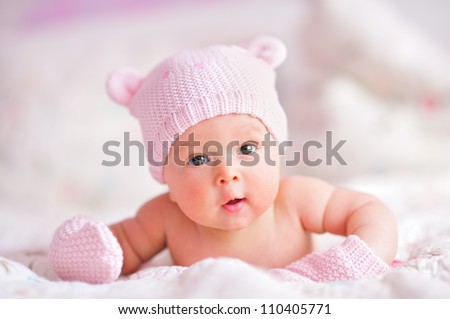 newborn baby girl in pink knitted bear hat and mittens on a bed