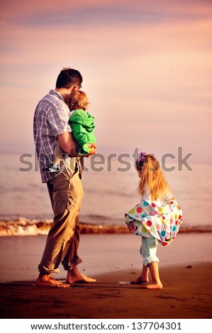 happy young family father and two daughters have fun on beach run and jump at sunset