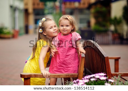 Two lovely little sisters outdoors in city at beautiful summer day hug and smile