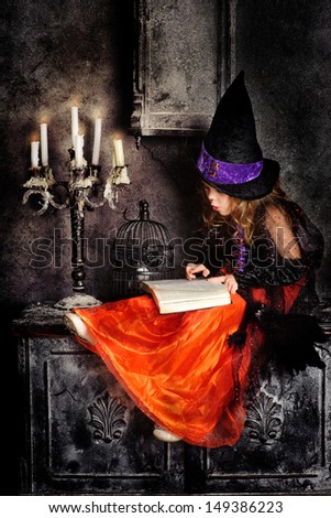 Little girl witch with a book in her hands and candles on halloween night