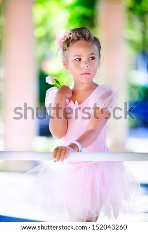 Little ballerina girl doing ballet bar exercises with flower on her hand at beautiful garden background
