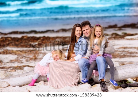portrait happy young family of four in casual fashion wear on a sandy beach at sunny summer day