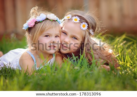 portrait of two happy adorable little  girls sisters on green grass at sunny summer day