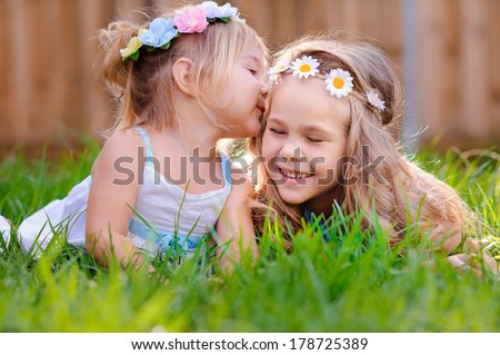 portrait of two happy adorable little girls sisters on green grass at sunny summer day