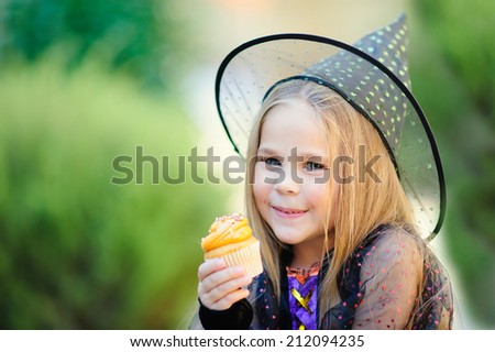 Happy Little girl wearing witch costume eat cupcake on Halloween