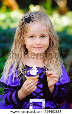happy little girl in which Halloween costume eat cupcake