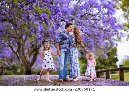 Happy Young beautiful family of mother, father and two little daughters in jacaranda blossom garden