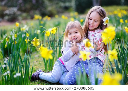 Cute happy little sisters hugging and having fun in spring meadow