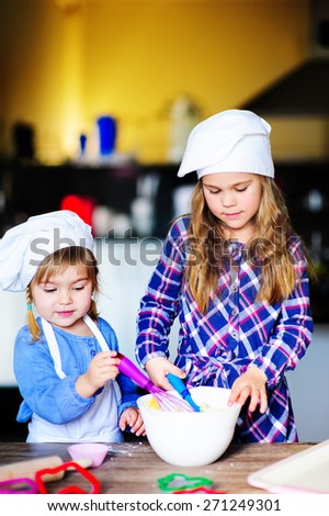 cute family of two girls wearing chef hats baking in the kitchen indoor
