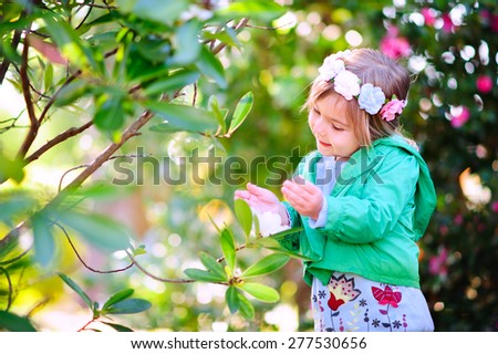 Cute toddler girl in fashion clothes at spring day smelling gardens flowers