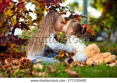 Cute little sisters hugging and kissing in autumn park